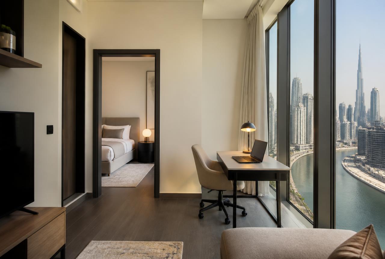 Furnished one-bedroom apartment interior in Business Bay with a work desk beside floor-to-ceiling windows overlooking the Dubai Water Canal and Burj Khalifa